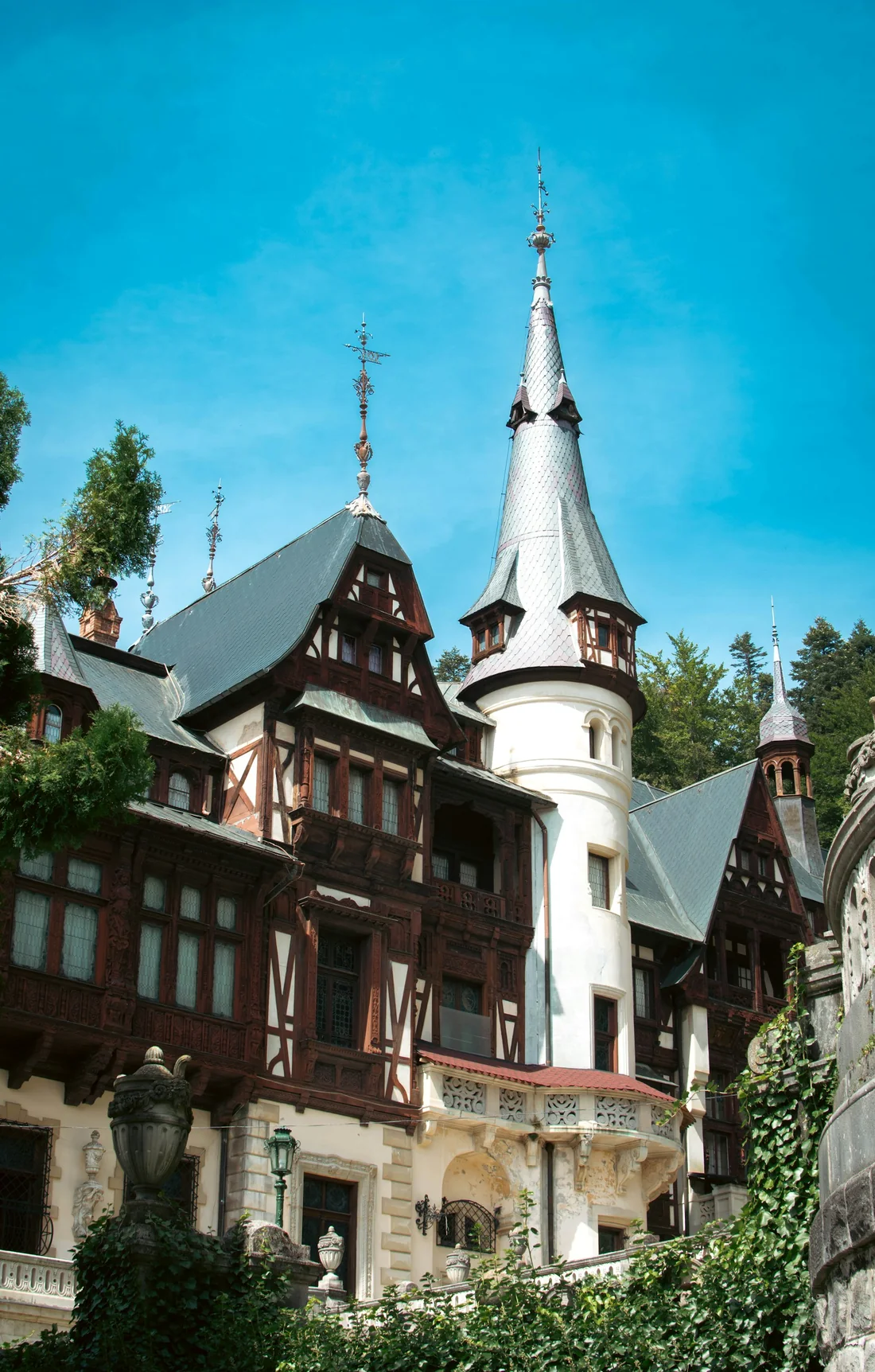 The spired towers and carved timber facades of Peleș Castle in Sinaia under a clear blue sky