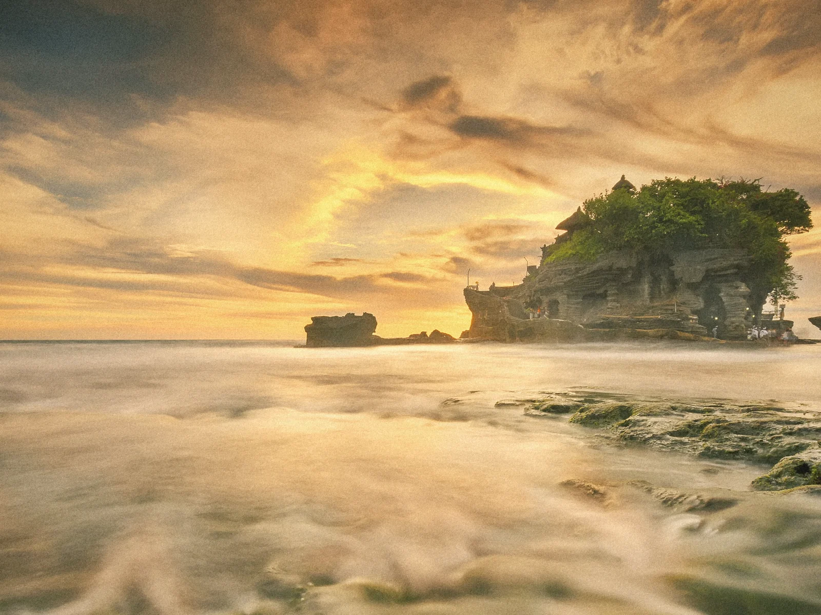 Tanah Lot sea temple on its rock at a golden sunset, waves washing over the shore