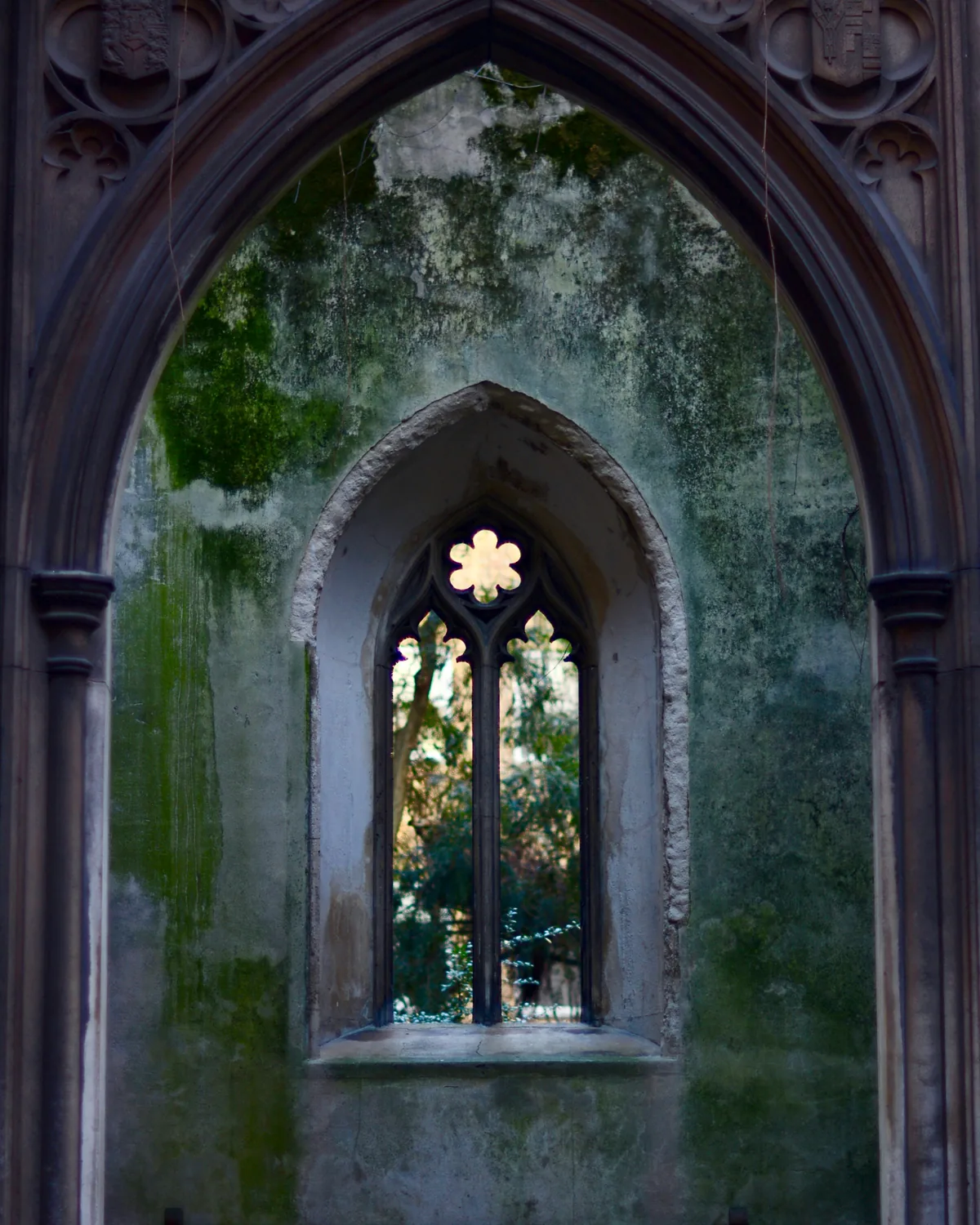 A gothic arched window and moss-covered stone walls inside the ruined church of St Dunstan in the East