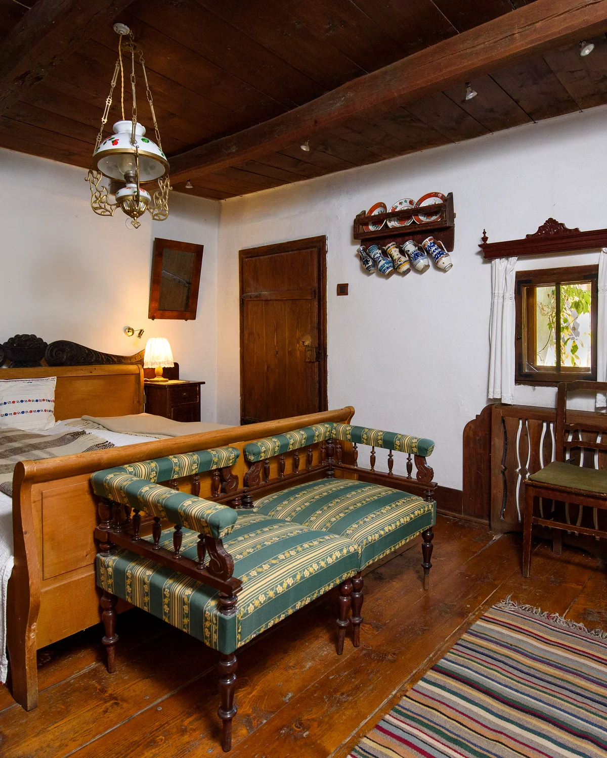 The Countess's room, with a painted green and white settee, a wooden bed, a beamed ceiling and a striped woven rug