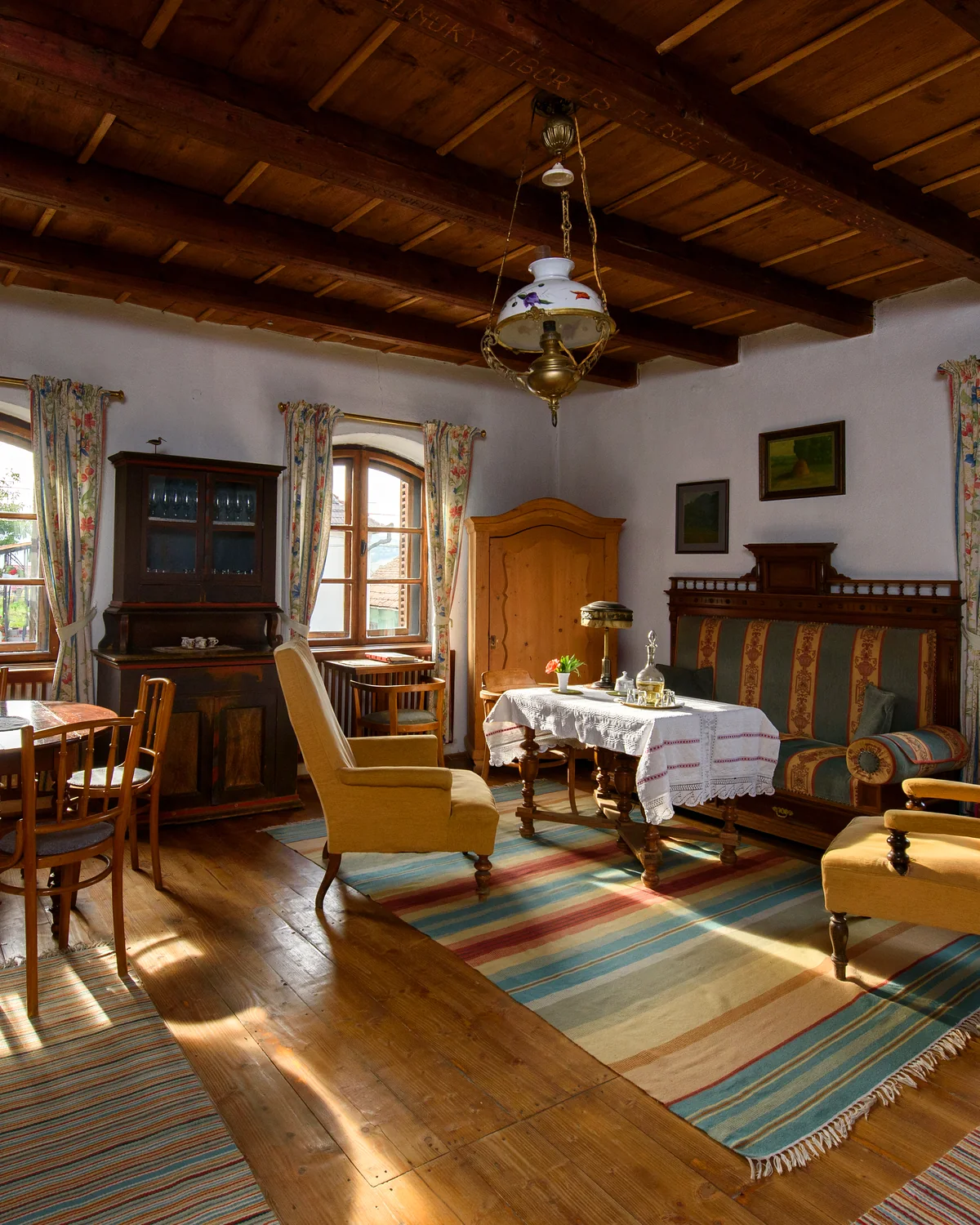 The drawing room of the main house, with antique armchairs, a set table, a tall wooden cabinet and striped rugs on wooden floors