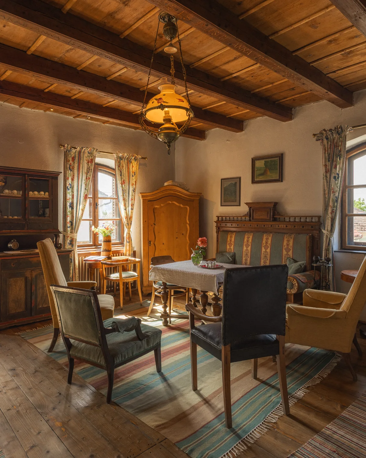 A guesthouse lobby with antique chairs, a round table, a wooden cabinet and a beamed ceiling