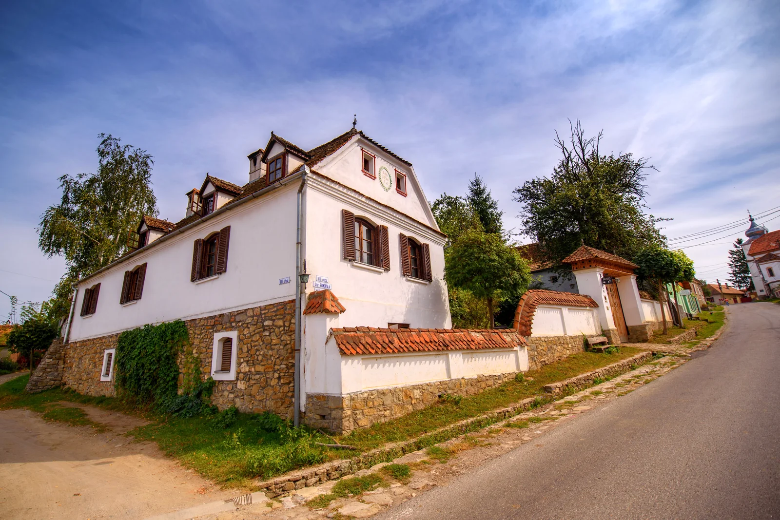 The long white main house at Count Kálnoky's seen from the village's main street, with a wooden gate and trees
