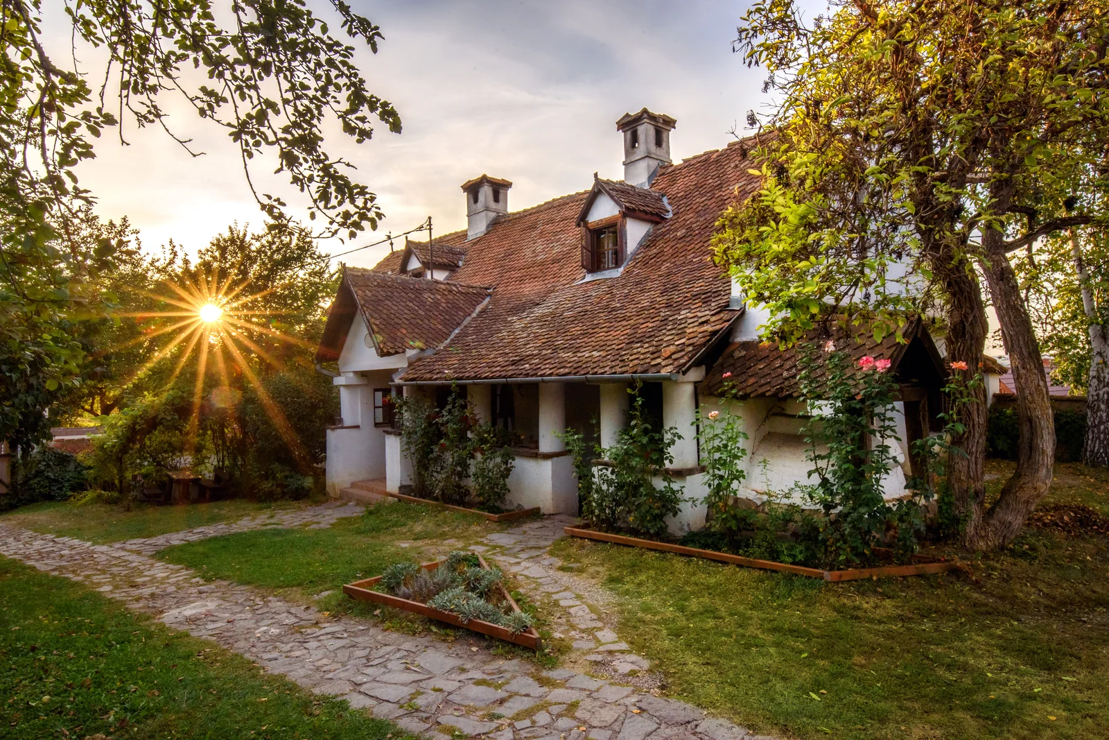 The whitewashed main house at Count Kálnoky's Guesthouses in Micloșoara at sunset, with a tiled roof, dormer windows and a cobbled garden path
