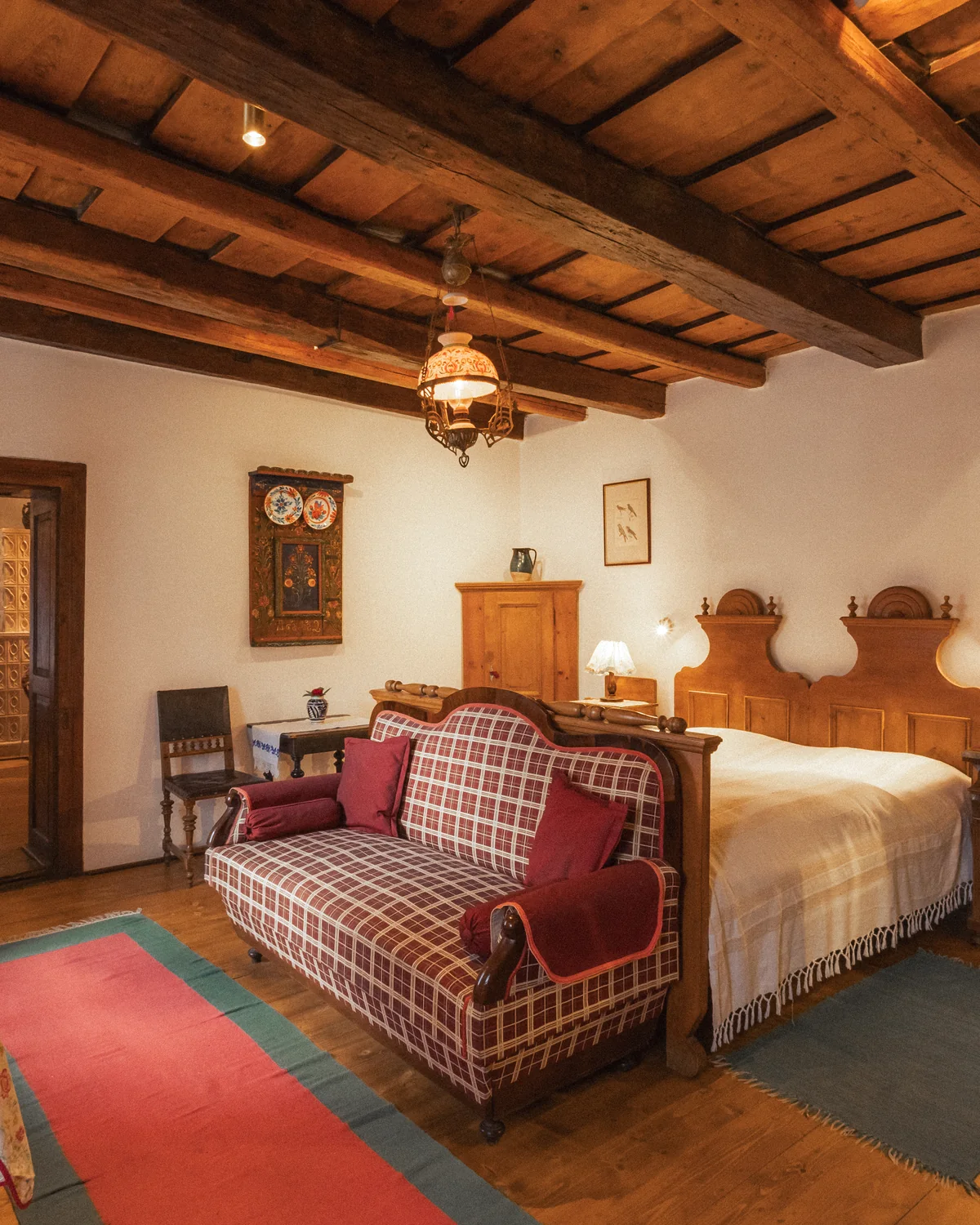 The Prince's Suite bedroom, with a carved wooden bed, a red tartan sofa, beamed ceiling and a hanging lantern