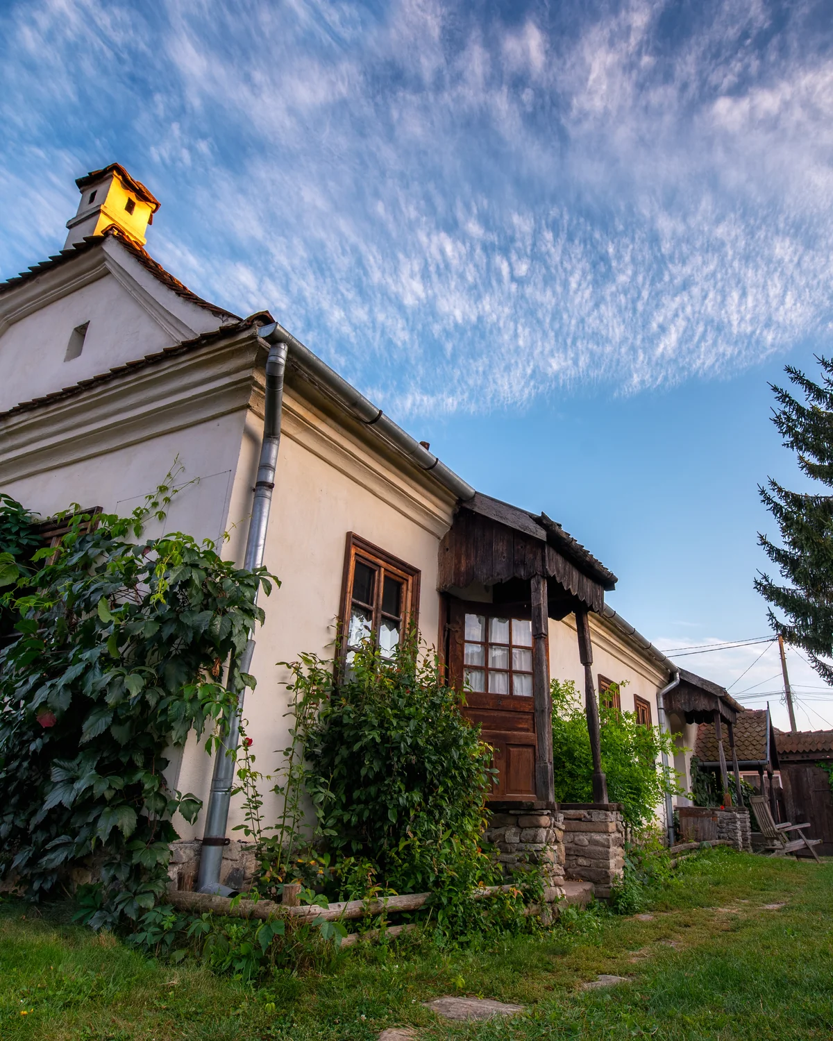 The Stucco House, a white cottage with a tiled roof and climbing greenery under a blue sky