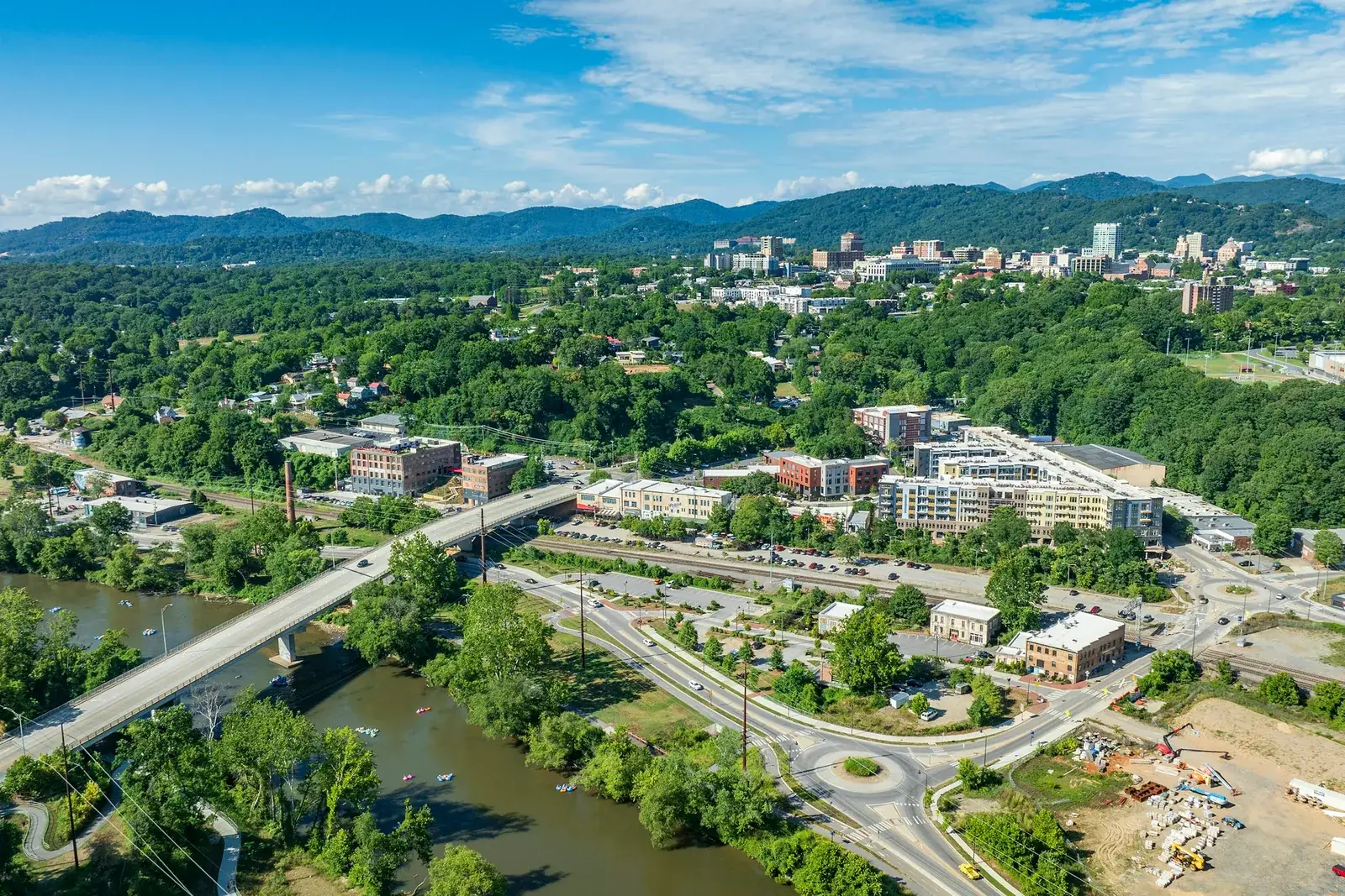 An aerial view of Asheville with the French Broad River winding past the city and the Blue Ridge on the horizon