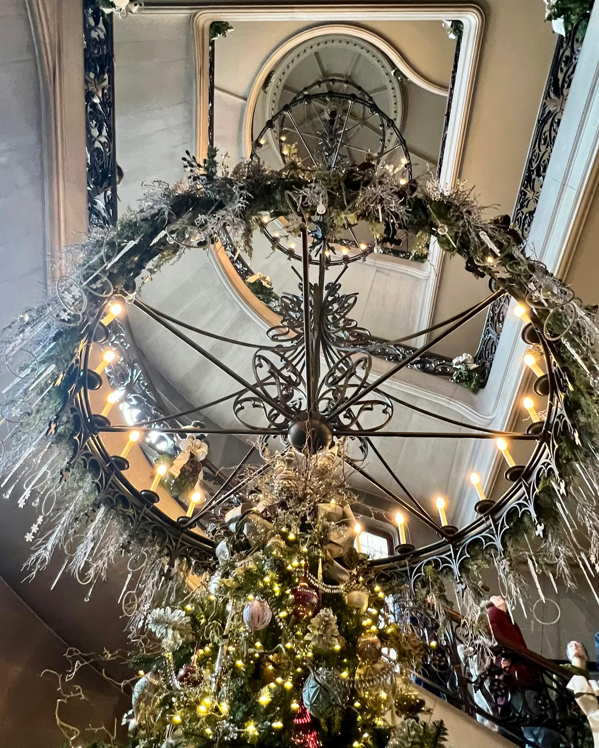 Looking up at the grand staircase and wrought-iron chandelier of Biltmore House, dressed in Christmas garlands above a lit tree