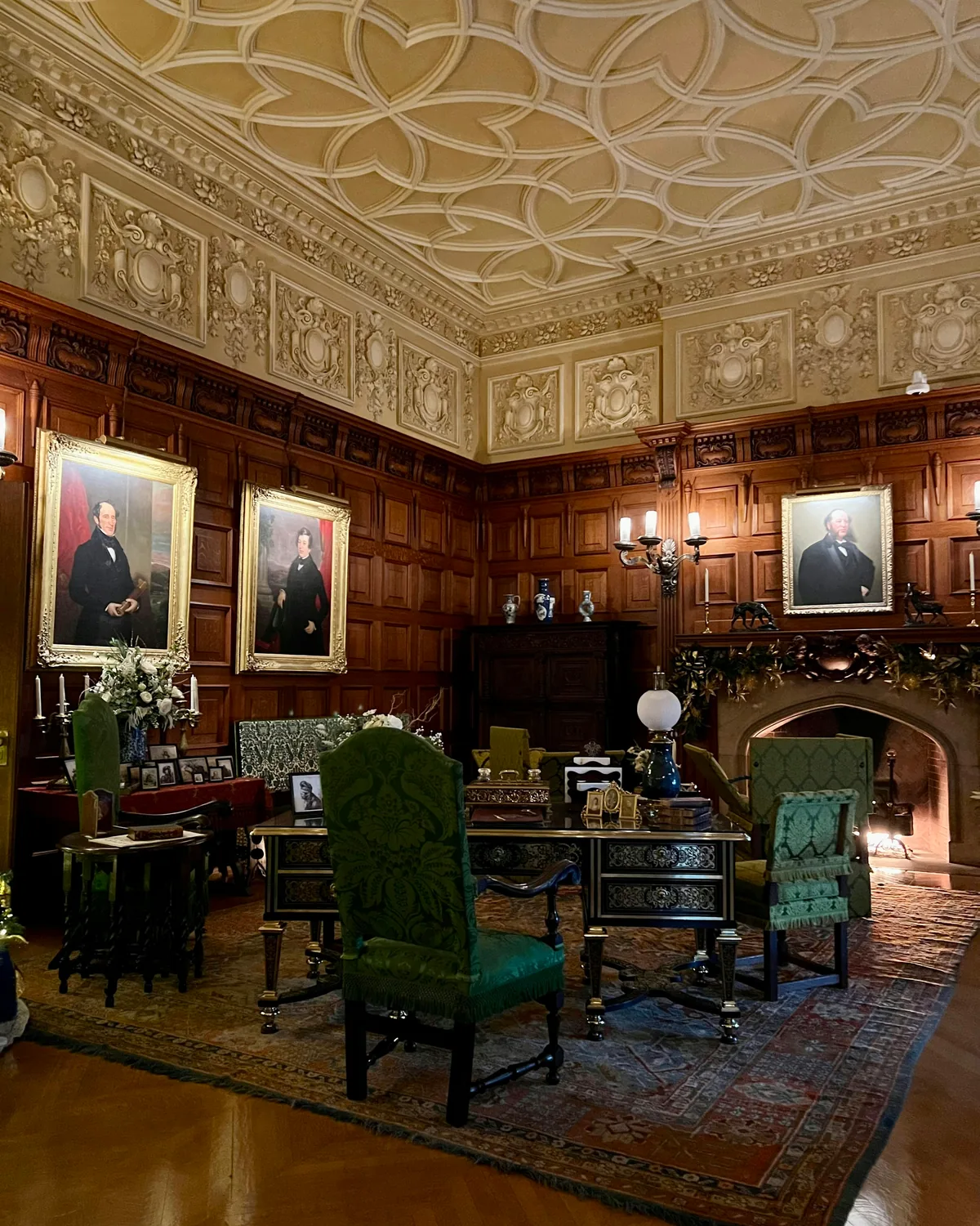 The wood-paneled Oak Sitting Room inside Biltmore House, with portraits, a carved ceiling and a stone fireplace