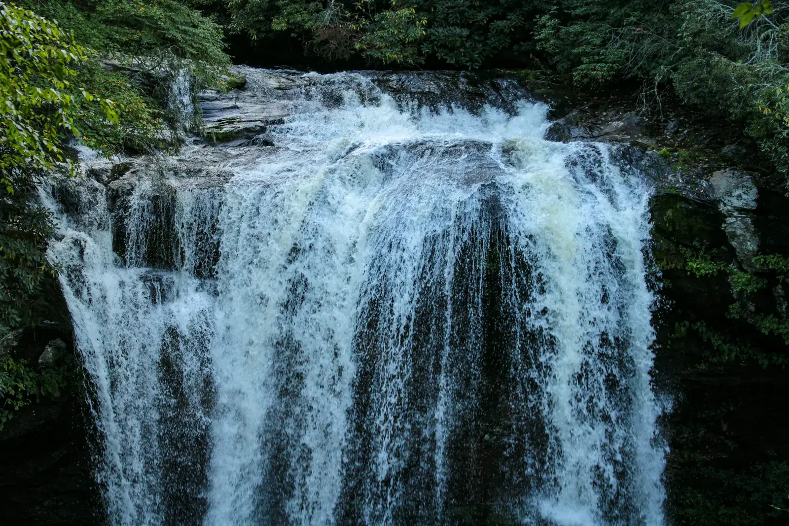 A powerful waterfall pouring over a rock ledge into a forest pool near Highlands