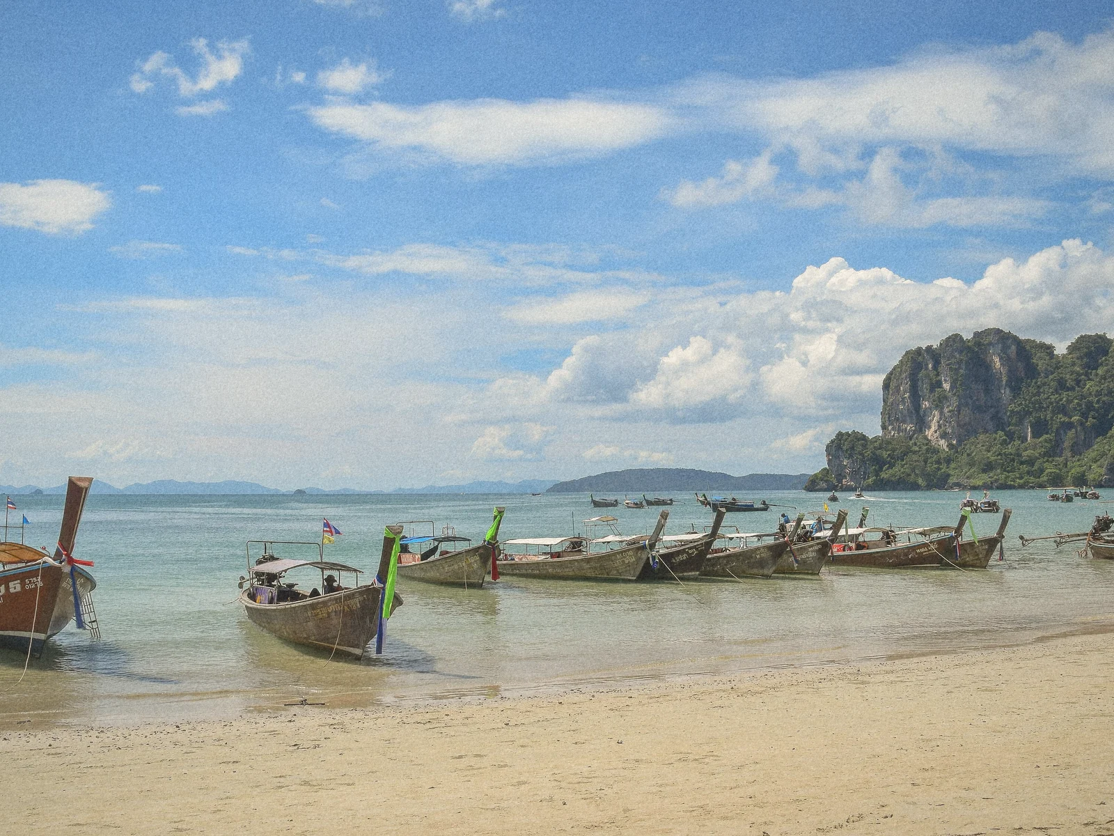 Longtail boats pulled up on Railay beach beneath limestone cliffs