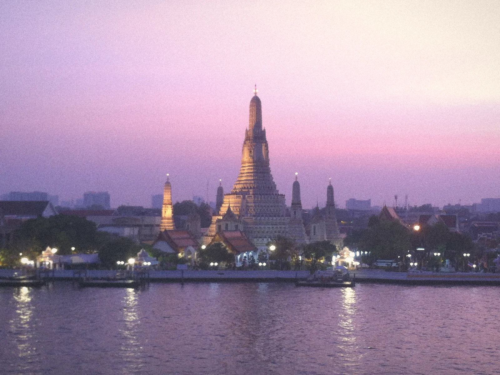 Wat Arun's spires lit up across the Chao Phraya river under a lavender dusk sky