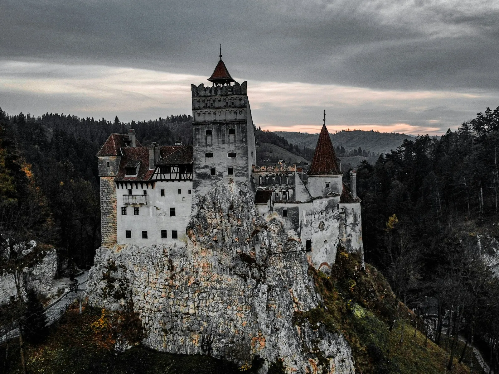 Bran Castle's white towers and red roofs on a rocky crag under heavy storm clouds