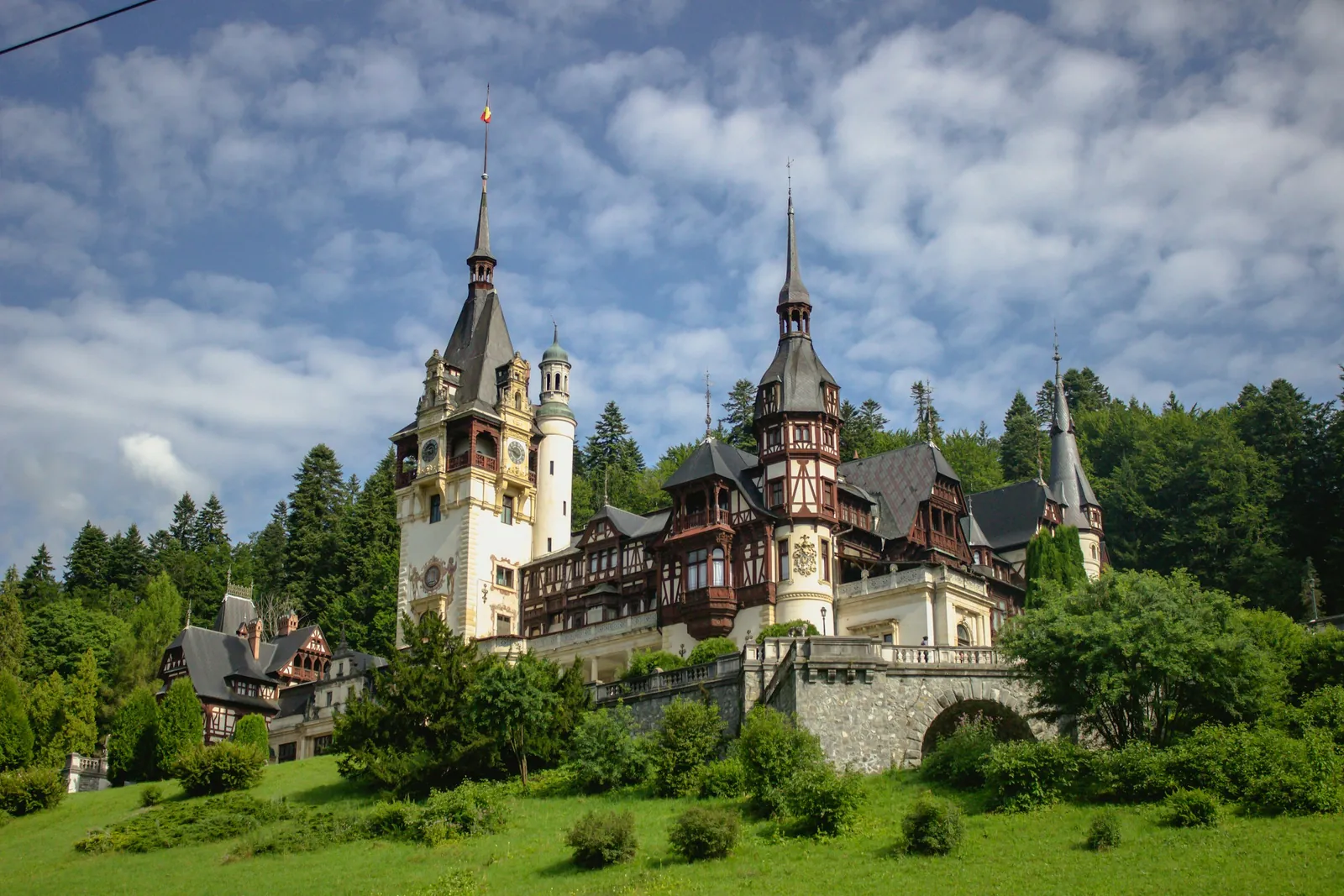 Peleș Castle's Neo-Renaissance towers and timbered facade on a wooded hillside in Sinaia