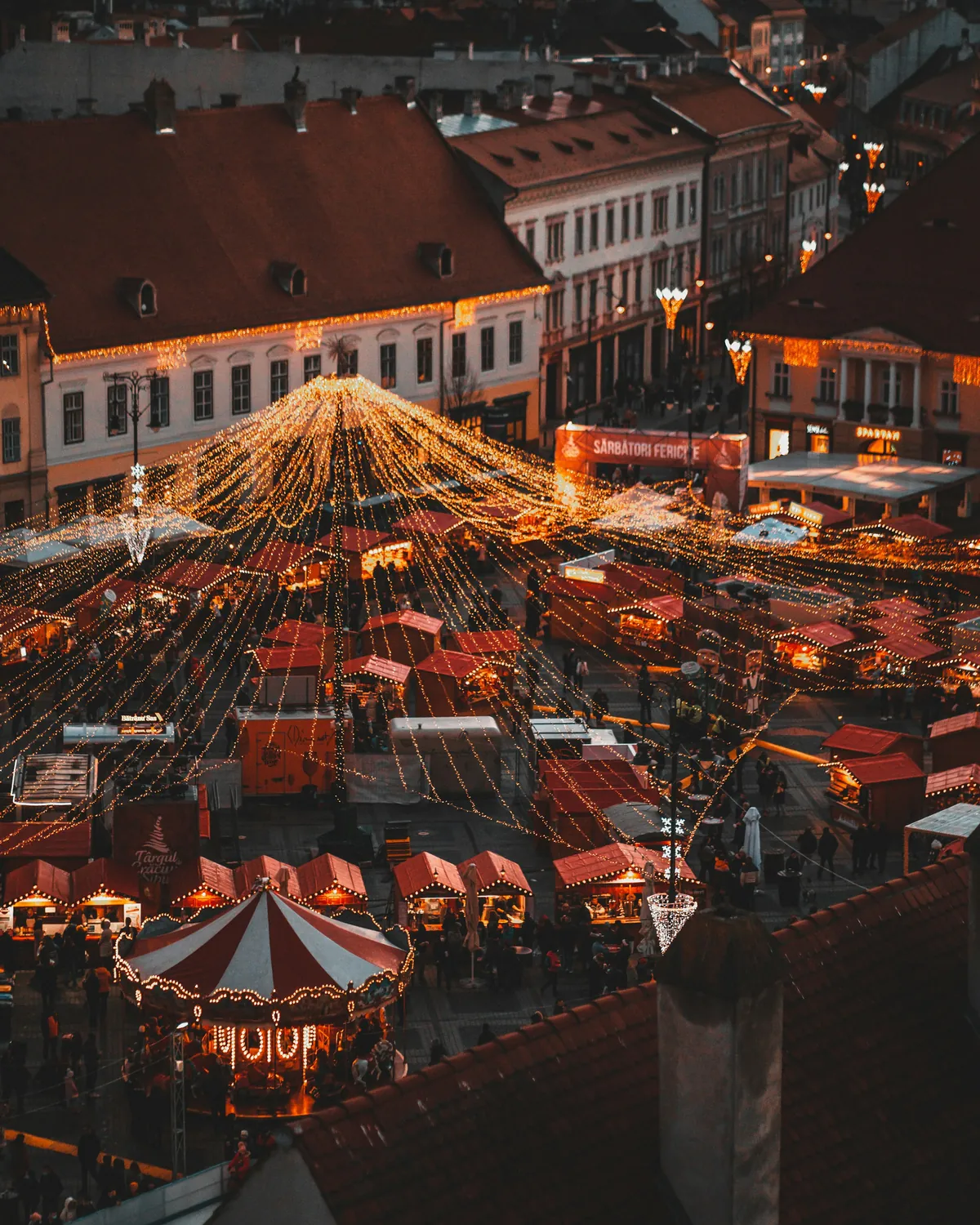Sibiu's main square at night filled with glowing Christmas market stalls and a tall lit tree