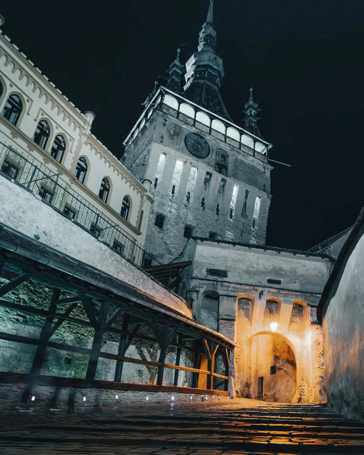 Sighișoara's Clock Tower lit up at night above the citadel walls and a covered stairway