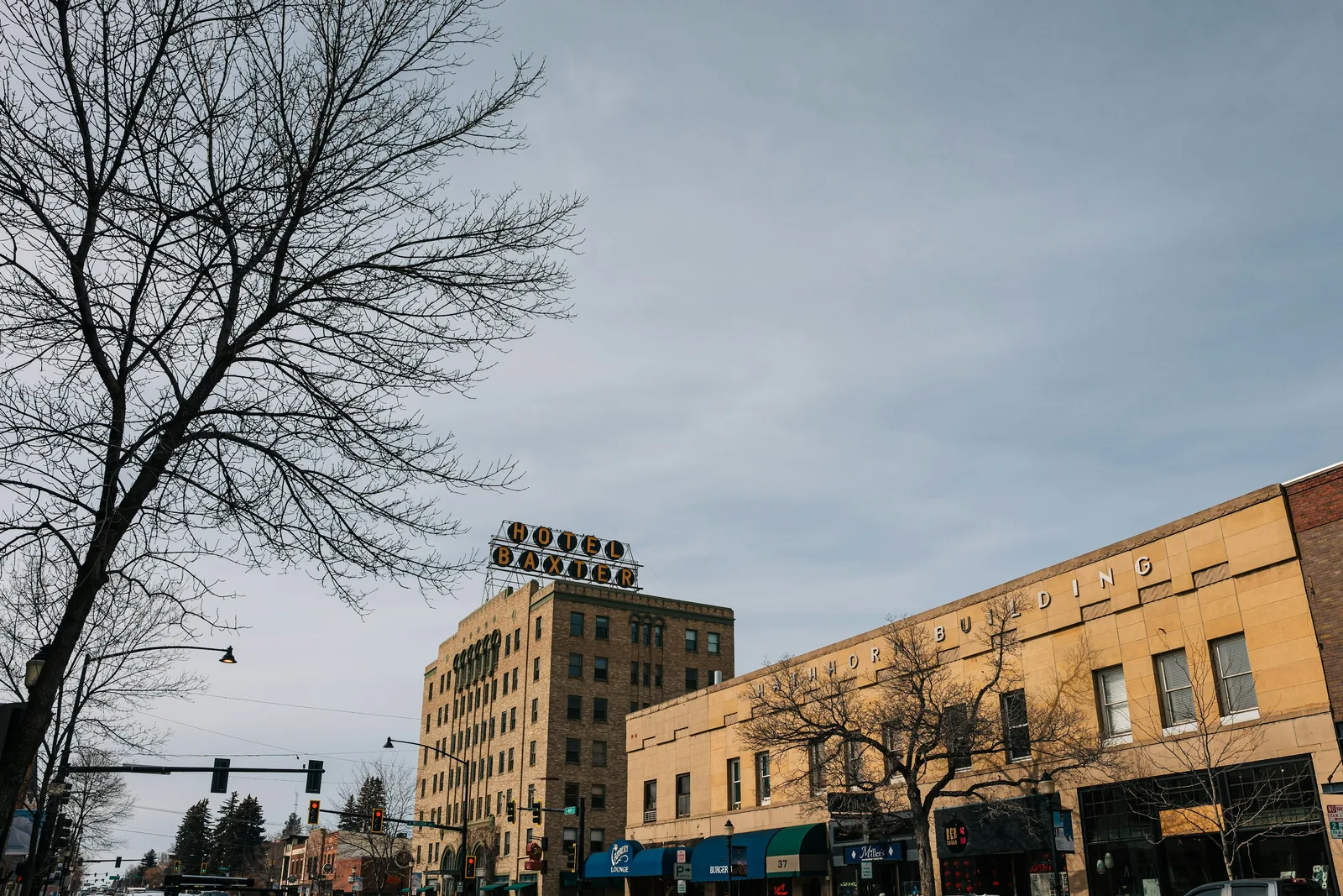 The Hotel Baxter's rooftop sign above the brick buildings of Main Street in downtown Bozeman, with bare winter trees