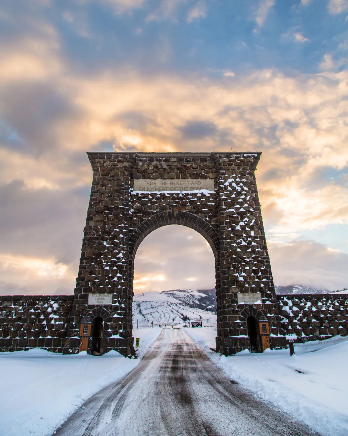 The stone Roosevelt Arch at Yellowstone's North Entrance at sunrise, with a snowy road running through it