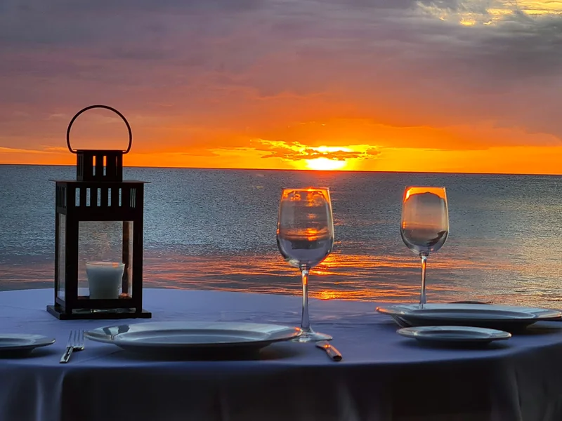 A candle lantern and two wine glasses on a table set for two by the sea at sunset