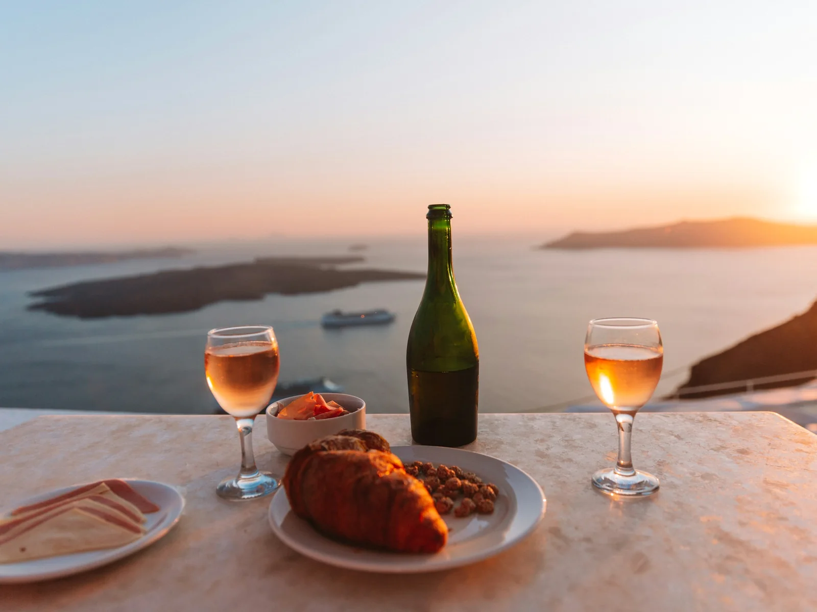 A simple table for two with wine, bread and two glasses above the sea at sunset