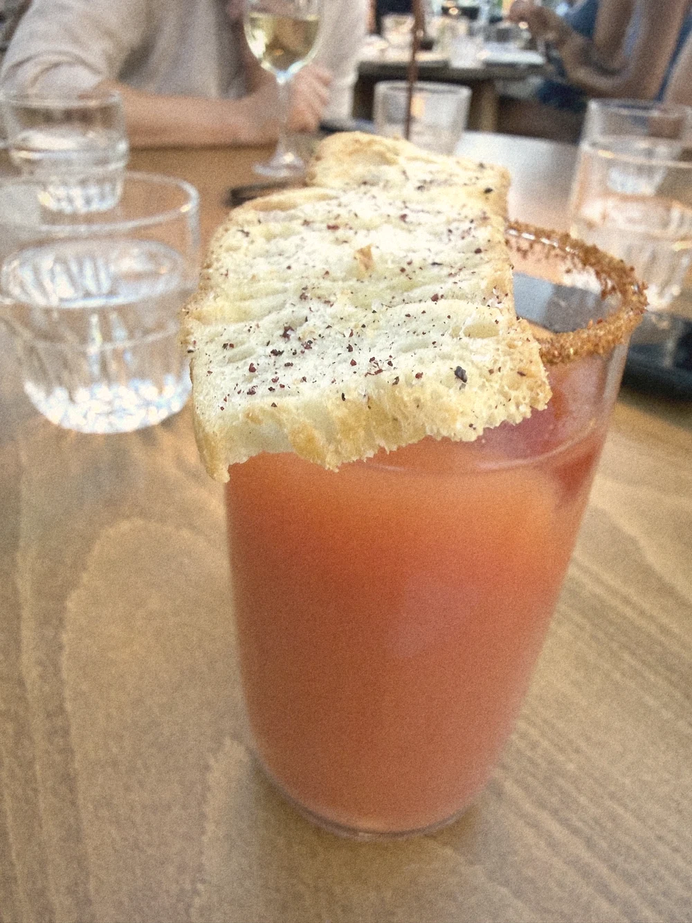 A red Chaos cocktail with a spiced rim and a large crispy bread cracker