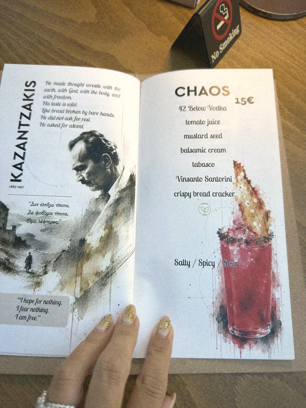 Attic's cocktail menu open at the Chaos page, paired with a portrait of Nikos Kazantzakis
