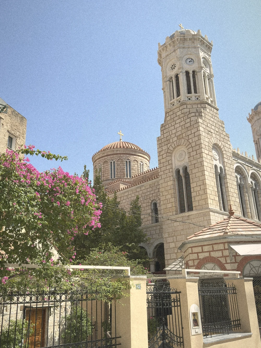 An ornate church with a clock bell tower and a tiled dome behind pink bougainvillea