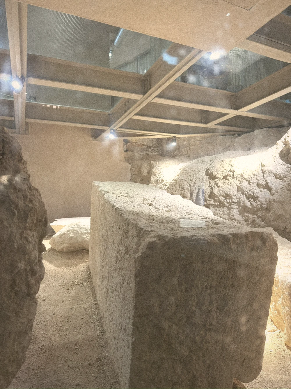 Ancient stone blocks lit softly beneath a glass floor and steel beams in the spa