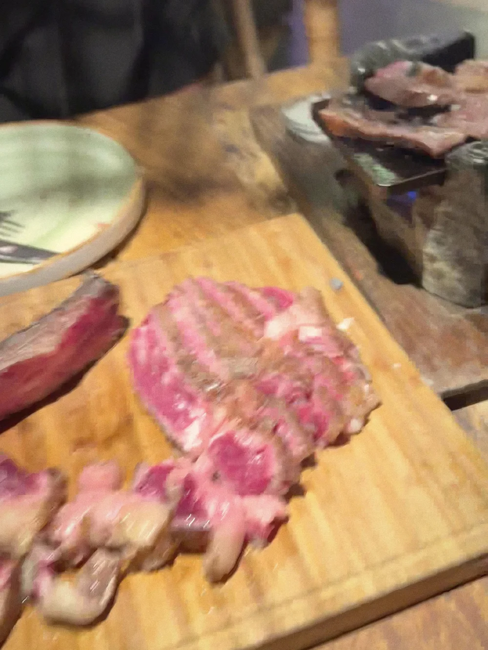 Sliced steak on a wooden board beside a hot stone grill at the table