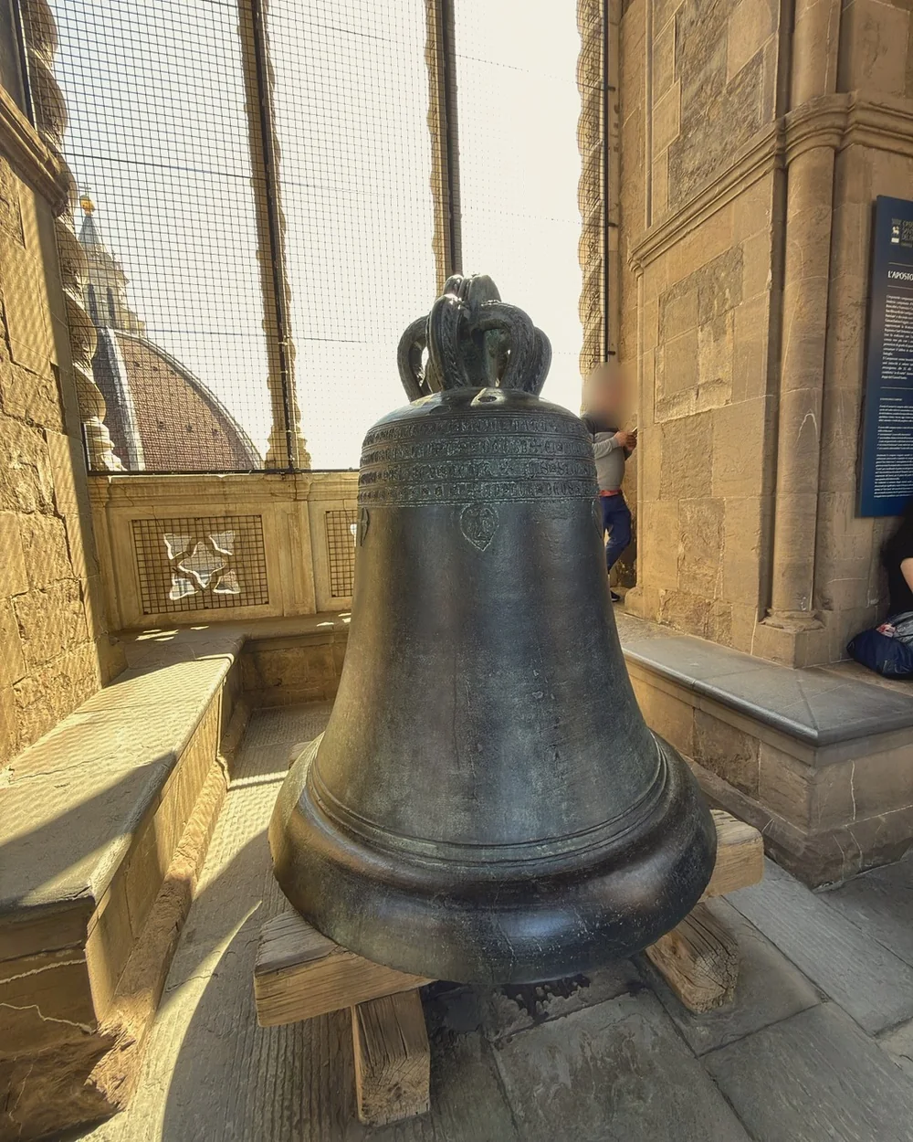 The great bronze Apostolic bell inside Giotto's bell tower, with Brunelleschi's dome visible through the window grille