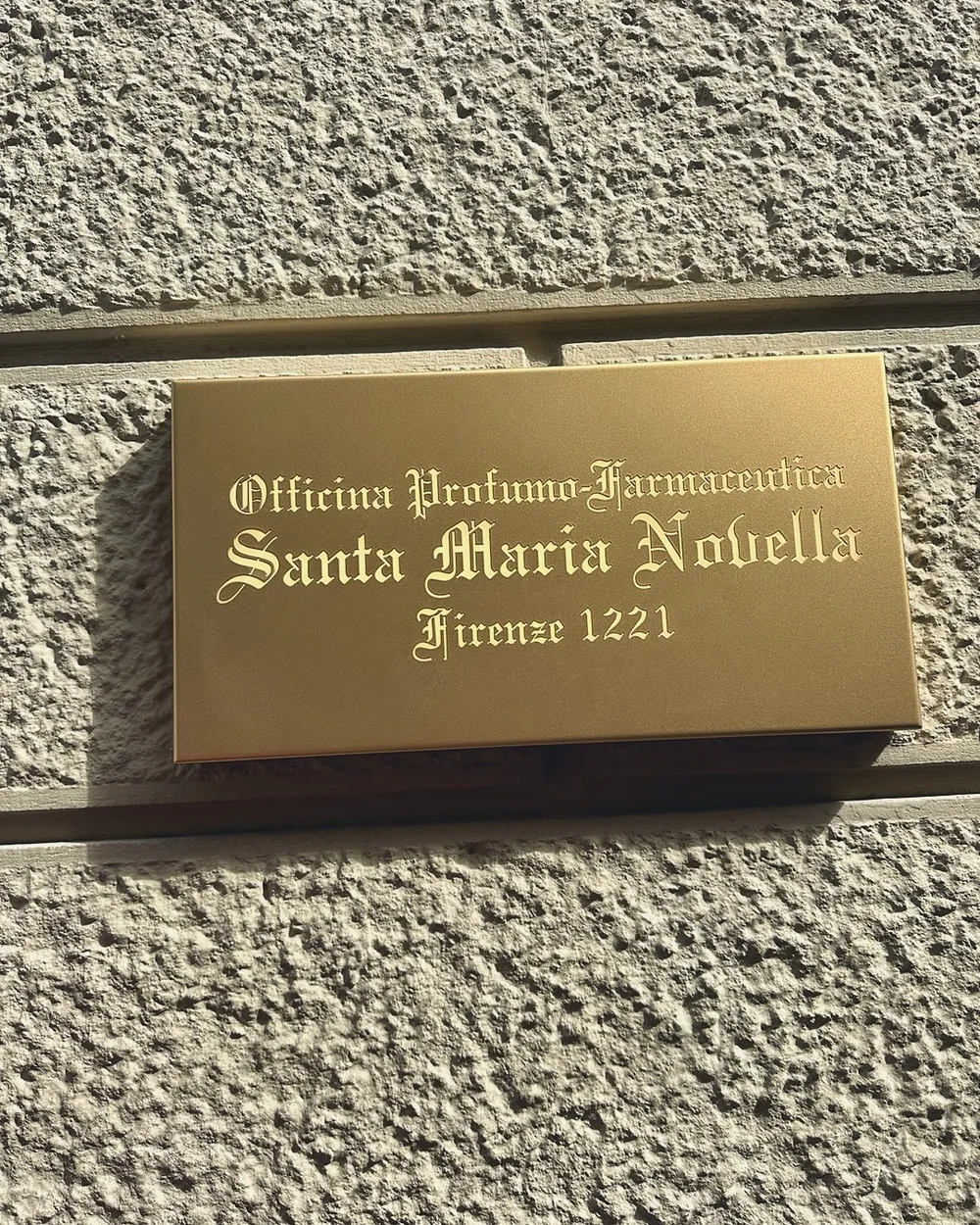 The brass plaque of the Officina Profumo-Farmaceutica di Santa Maria Novella, Firenze 1221, on a stone wall