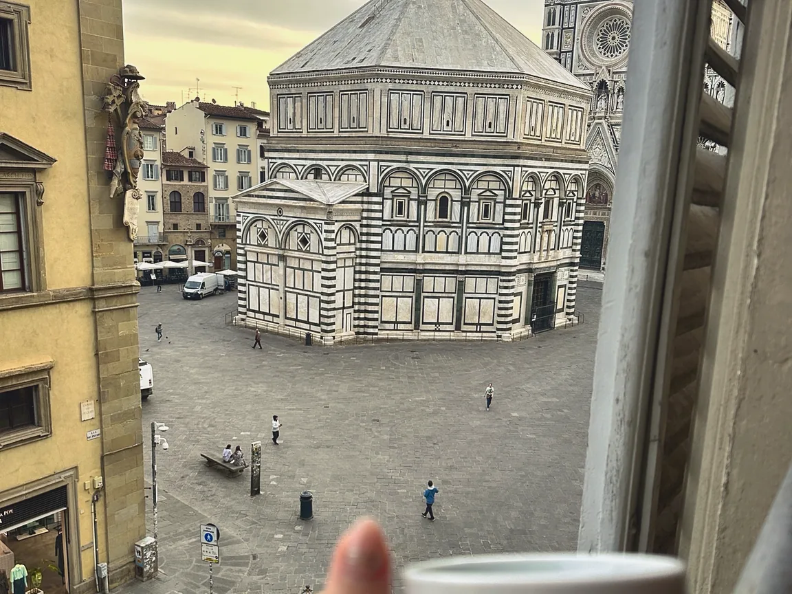 An espresso cup held at an open window above the Baptistery and Piazza San Giovanni in Florence
