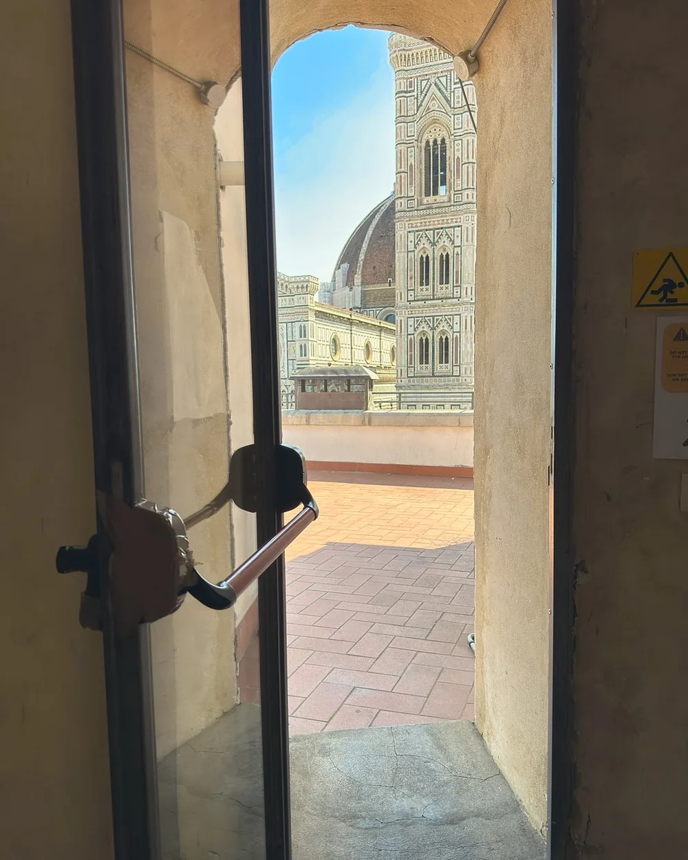 An open door onto a rooftop terrace with the Duomo's dome and Giotto's bell tower beyond