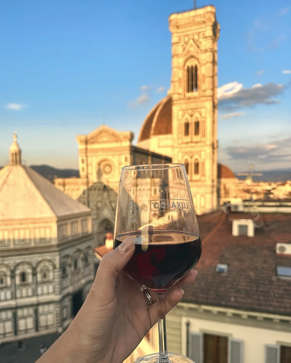 A glass of red wine raised towards the Duomo and Giotto's bell tower at sunset