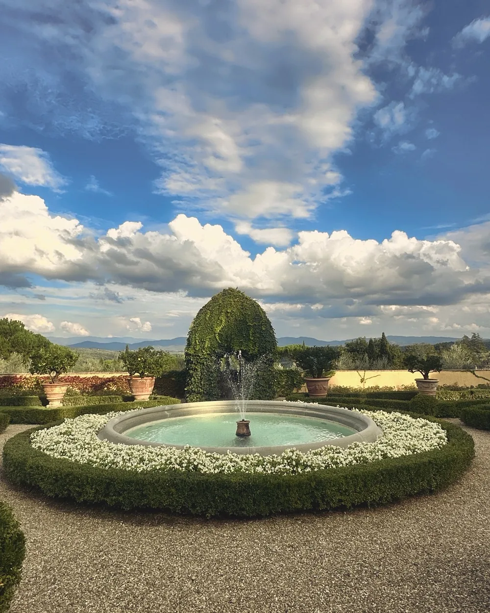 A round fountain in the formal garden at Villa Poggio Torselli under a big blue sky