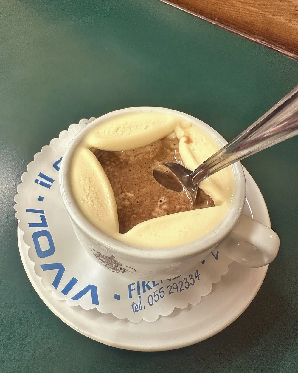 An affogato in a Vivoli cup and saucer, espresso poured over the gelato, on a green table