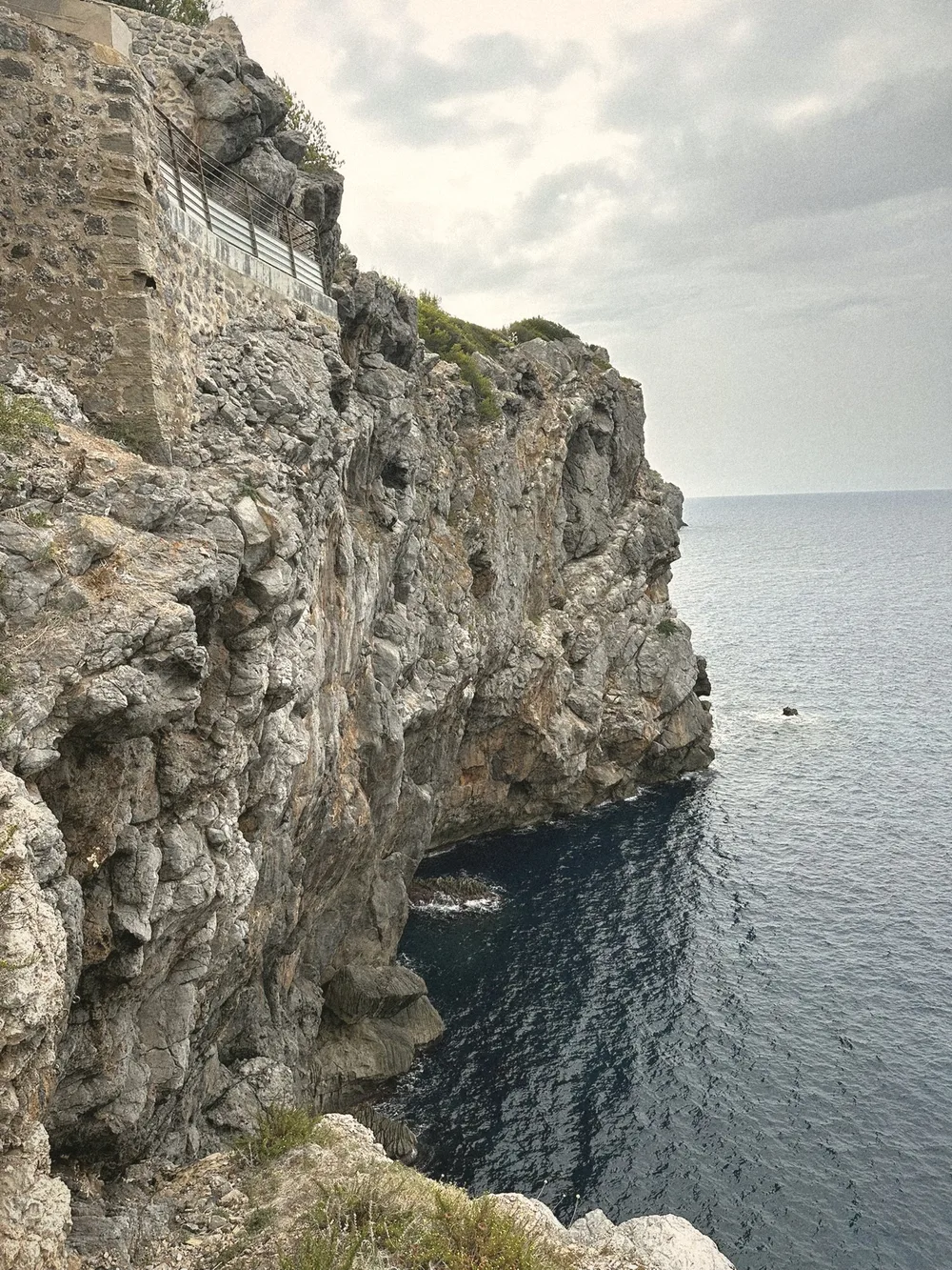 Steep limestone cliffs dropping into a deep blue, calm sea