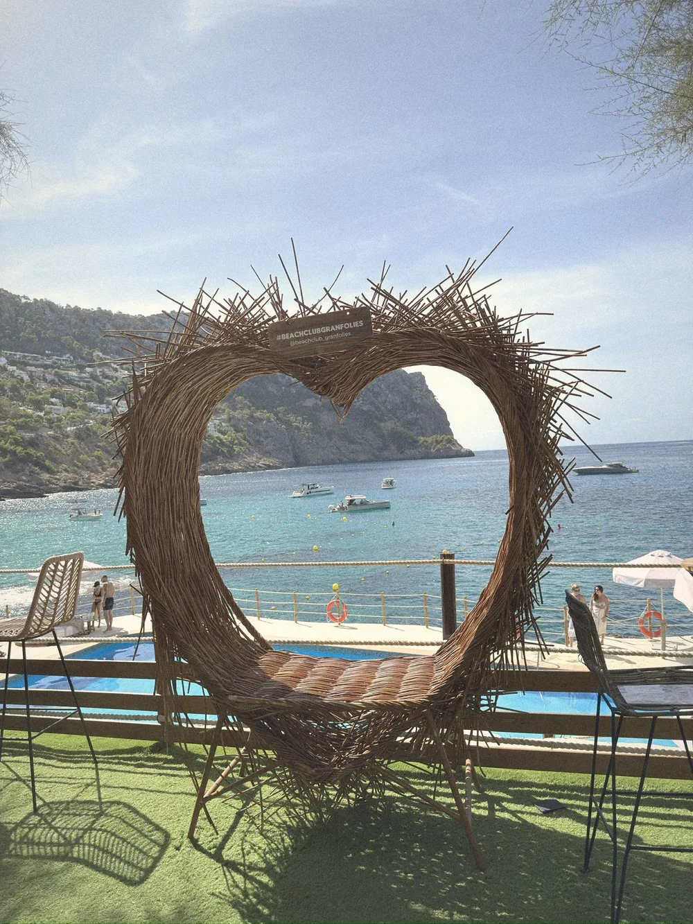 A woven wicker heart-shaped seat on the lawn, framing the bay and the hills through its centre
