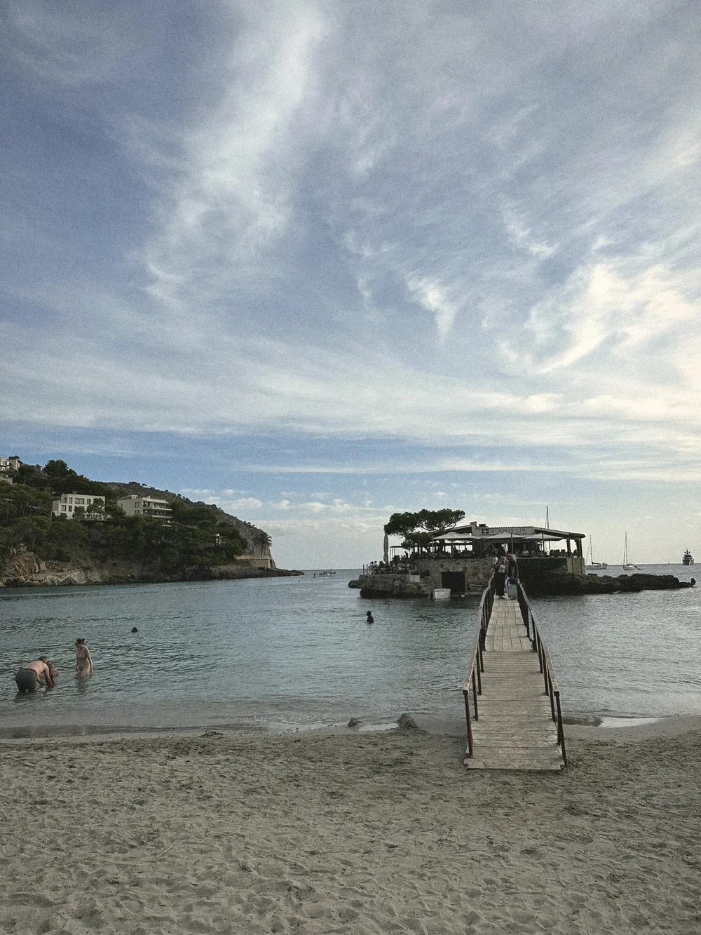A long wooden footbridge running from the beach across calm water to the small island of Restaurant Illeta