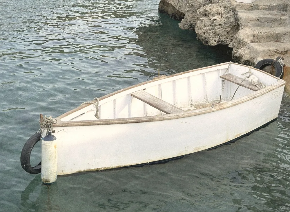 A little white wooden rowing boat moored against the rocks in clear green water