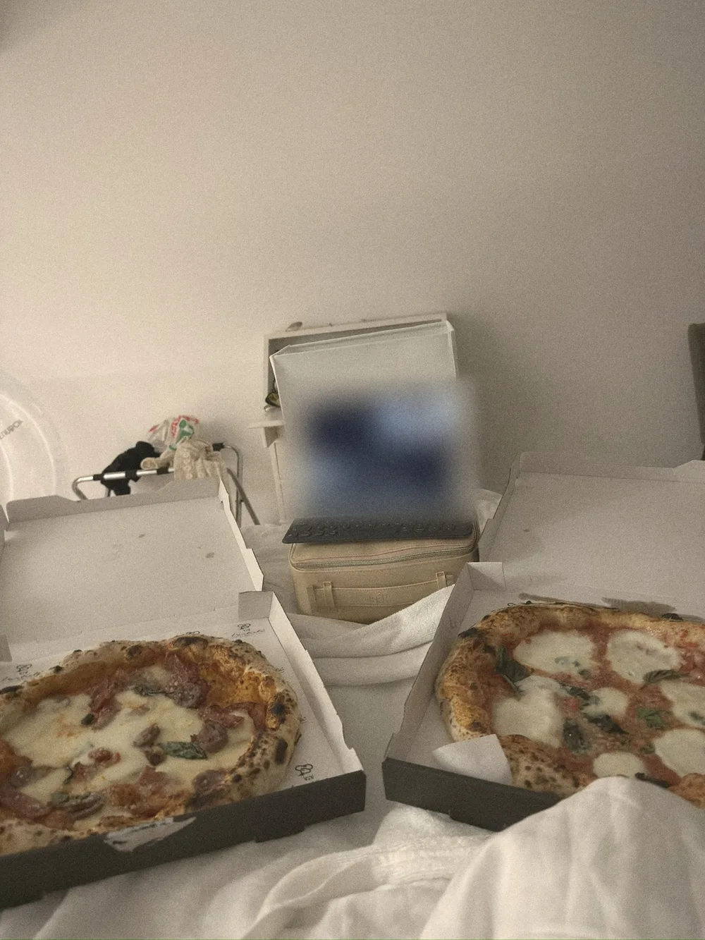 Two pizzas in open boxes on a bed, with a tablet propped on a beige Béis case for a movie night