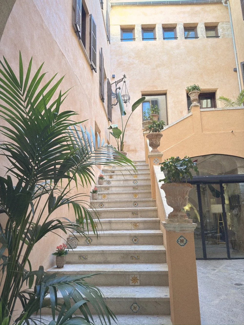 A stone staircase with tiled risers climbing an apricot courtyard wall, with potted palms and plants