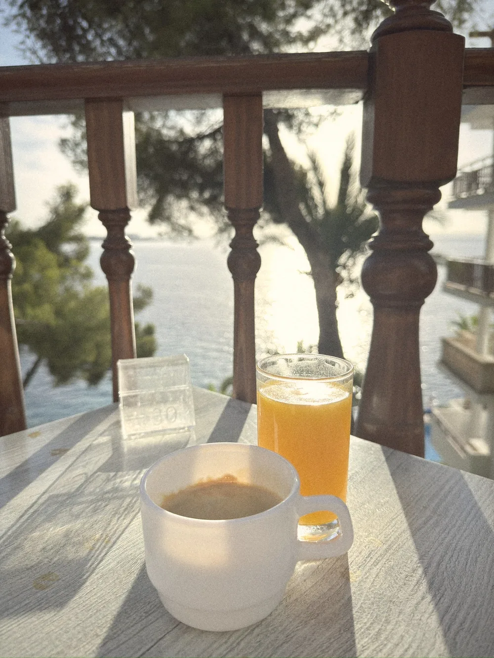 An espresso and a glass of fresh orange juice on our balcony table at Hotel ROC Illetas, with pines and the sea through the wooden railings