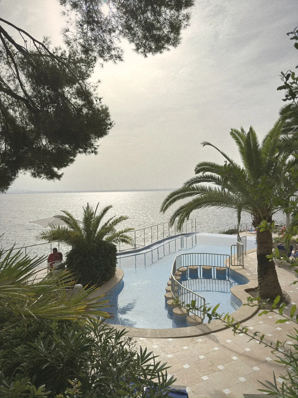 The curving seaside pool at Hotel ROC Illetas, with a swim-up bar, palm trees and the sea glittering beyond