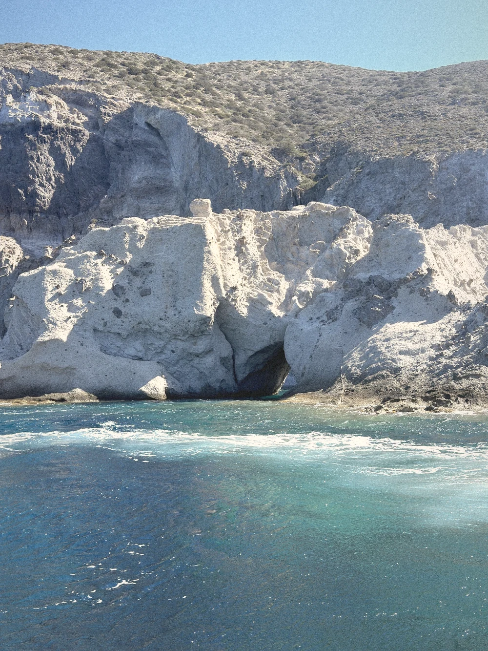White rock cliffs with a sea cave at the waterline and deep blue water