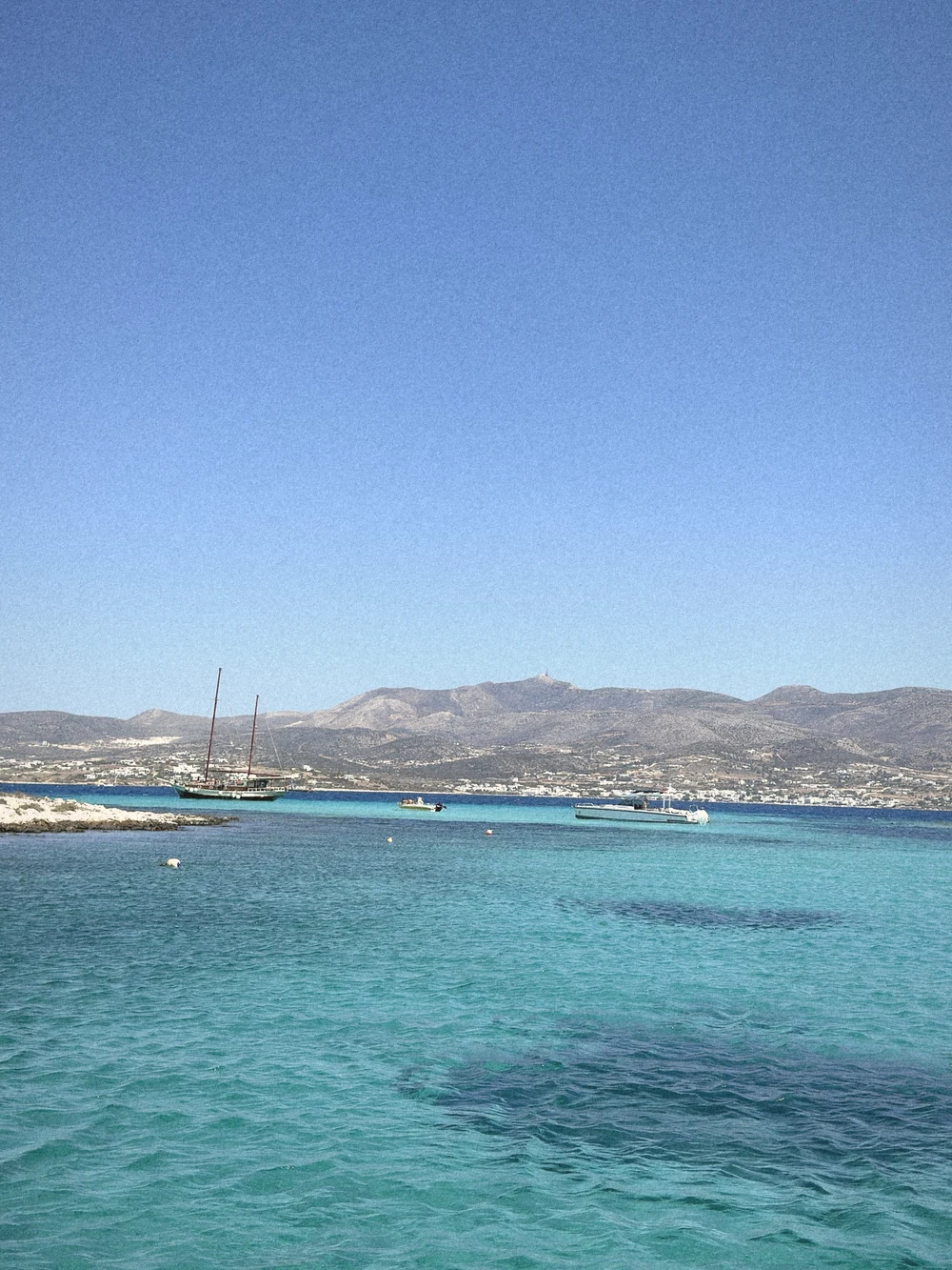 Bright turquoise shallows with sailboats anchored off a low island