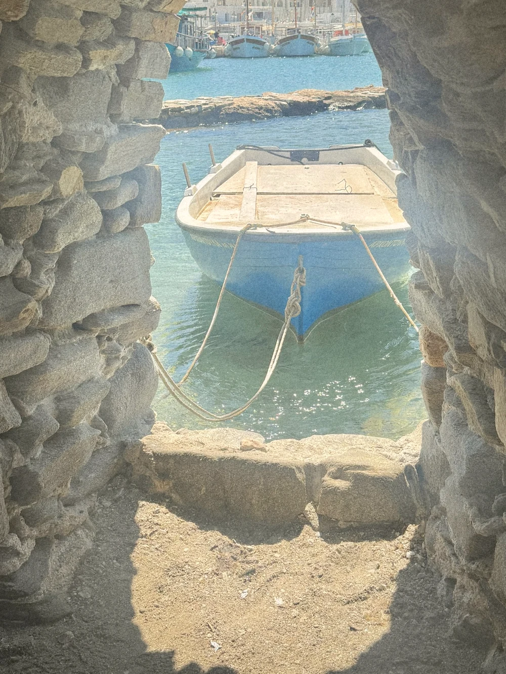 A pale blue wooden fishing boat moored in clear water, framed by a stone window in the castle wall