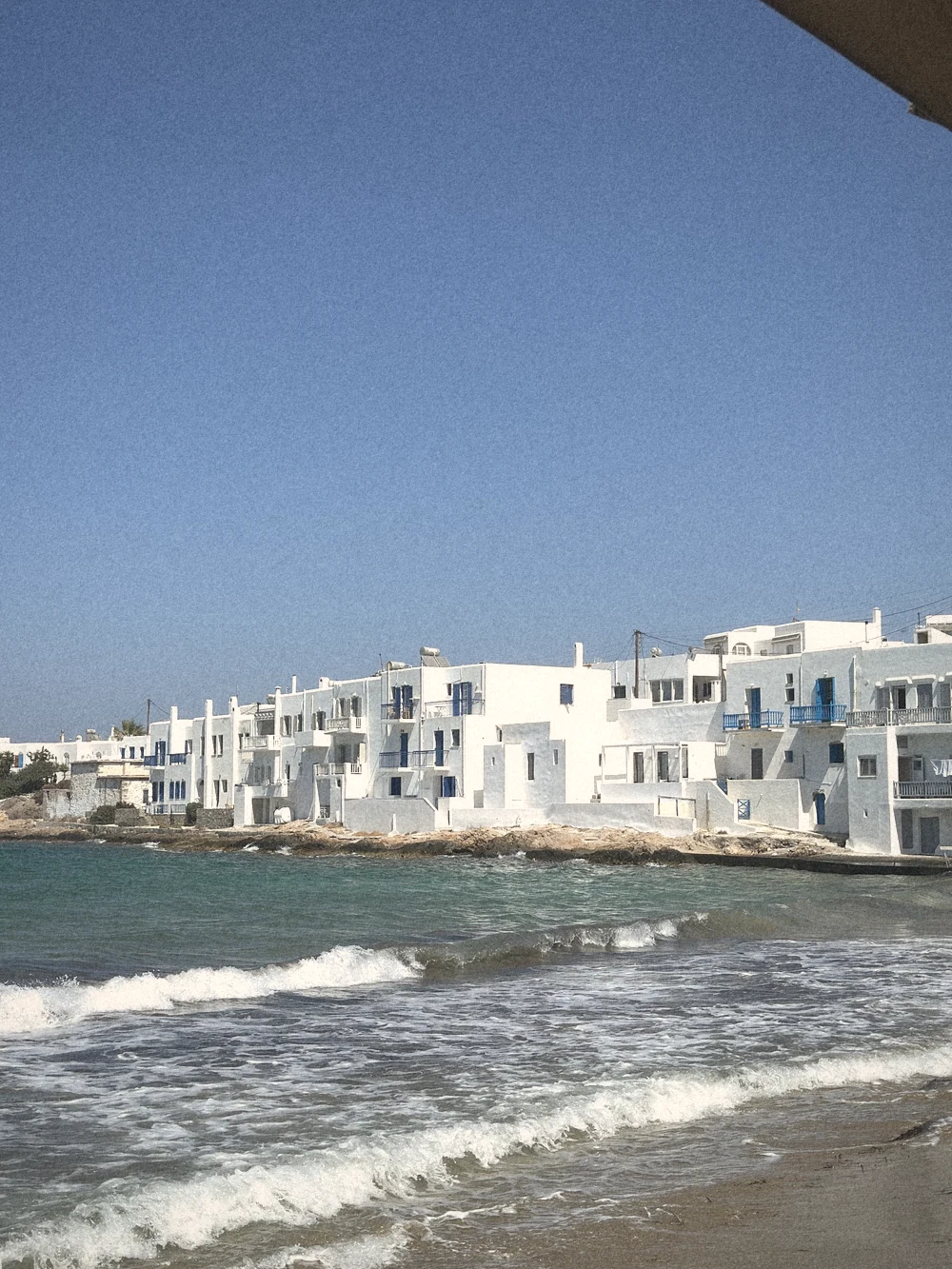 Whitewashed houses along Naoussa's waterfront with small waves rolling in