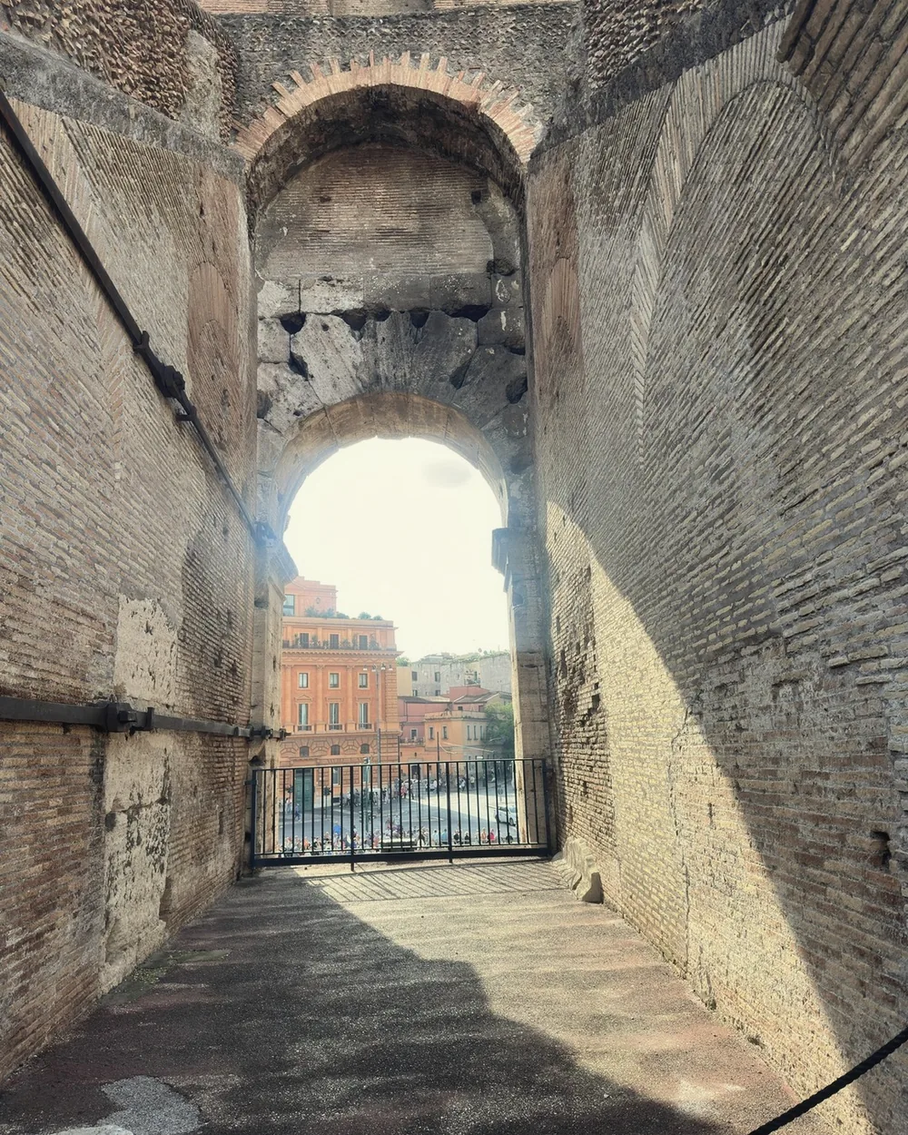 A sunlit brick corridor inside the Colosseum opening onto an arch