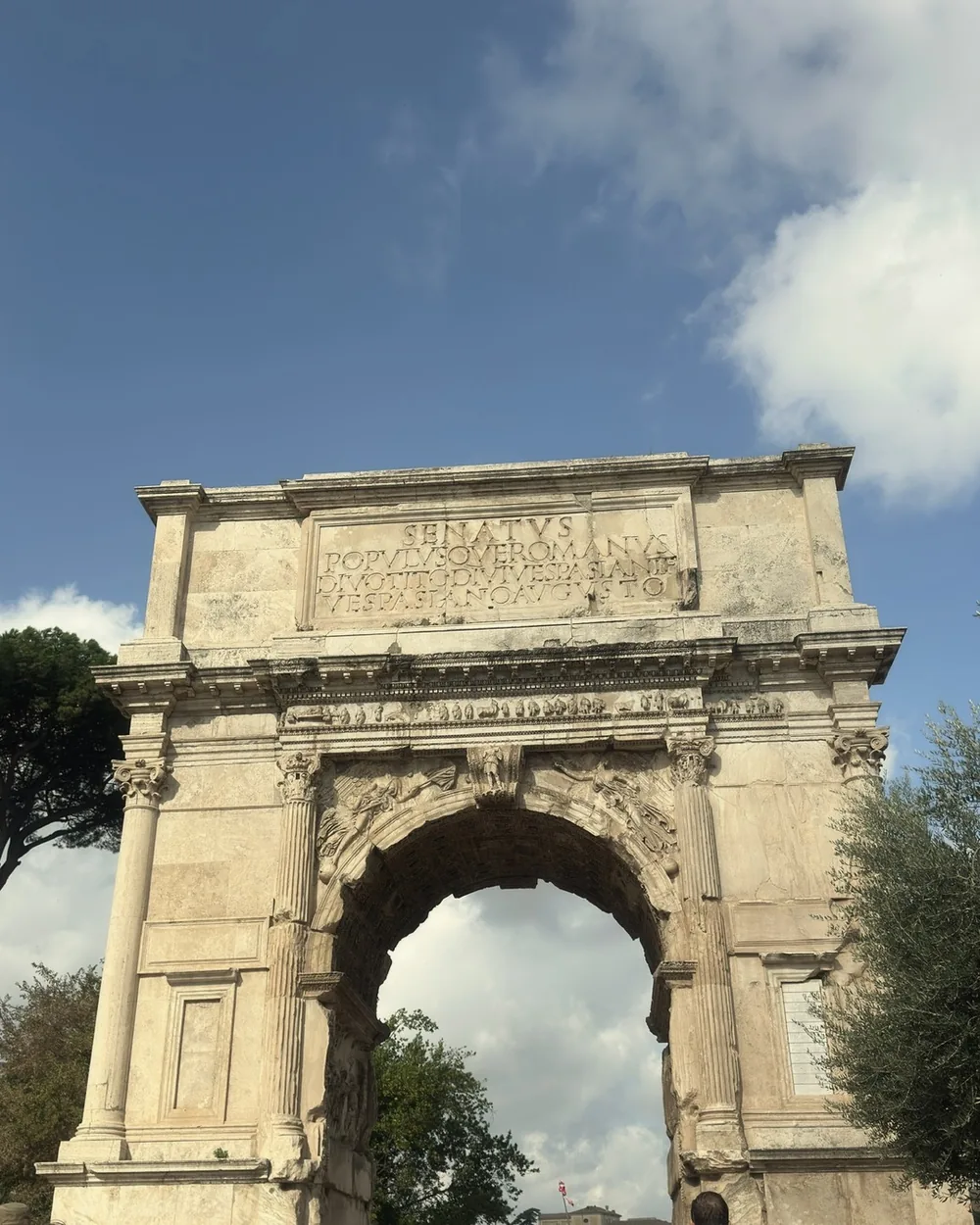 The Arch of Titus against a blue sky with soft white clouds